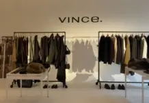 Vince expands into multi-brand retail platform with OVO deal Interior of a Vince showroom with two clothing racks, tables, and coats on display under the Vince sign at the back.