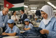 The Jordan Garment Industry Boosts Global Export Standards Female worker in a blue uniform folds denim jeans in a busy garment factory; a Jordan flag hangs in the background.