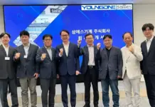 Youngone Corporation Partners with Sam Sung Machinery for Global Expansion Group of nine professionals in suits posing with fists raised in a conference room, blue display behind them.