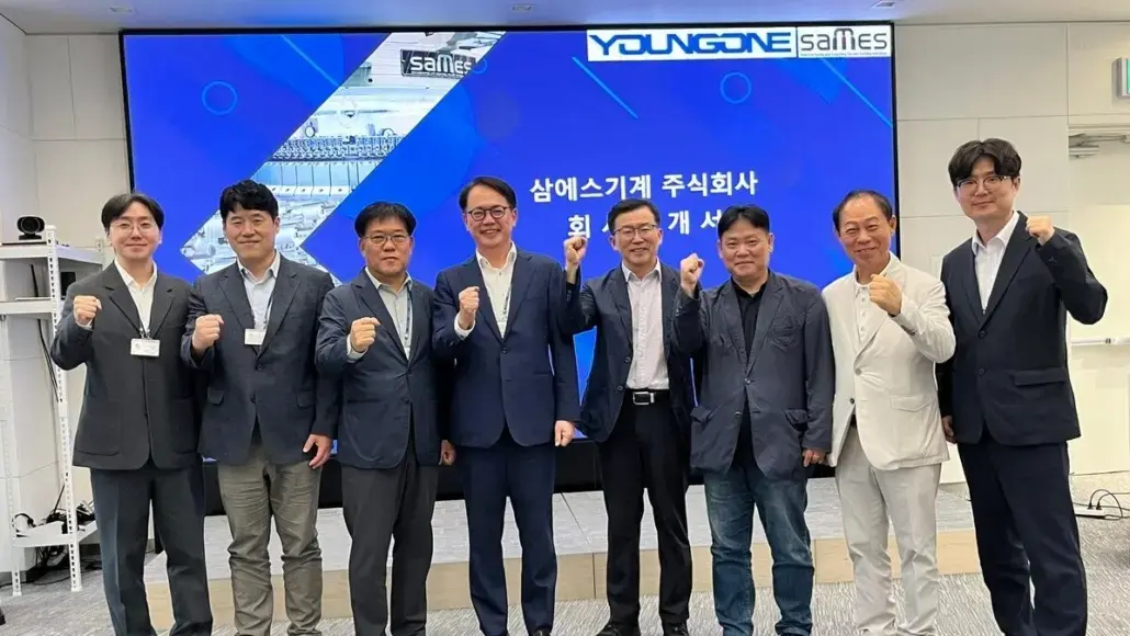 Group of nine professionals in suits posing with fists raised in a conference room, blue display behind them.