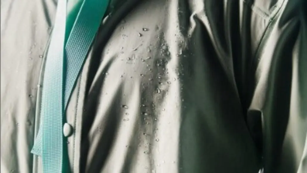 Close-up of a raincoat with water droplets on gray fabric and a teal strap visible behind.