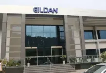 Gildan Advances Next Phase of HanesBrands Integration Strategy Front view of a modern Gildan office building with large glass doors, steps, and landscaped planters; a person walks by on the left.