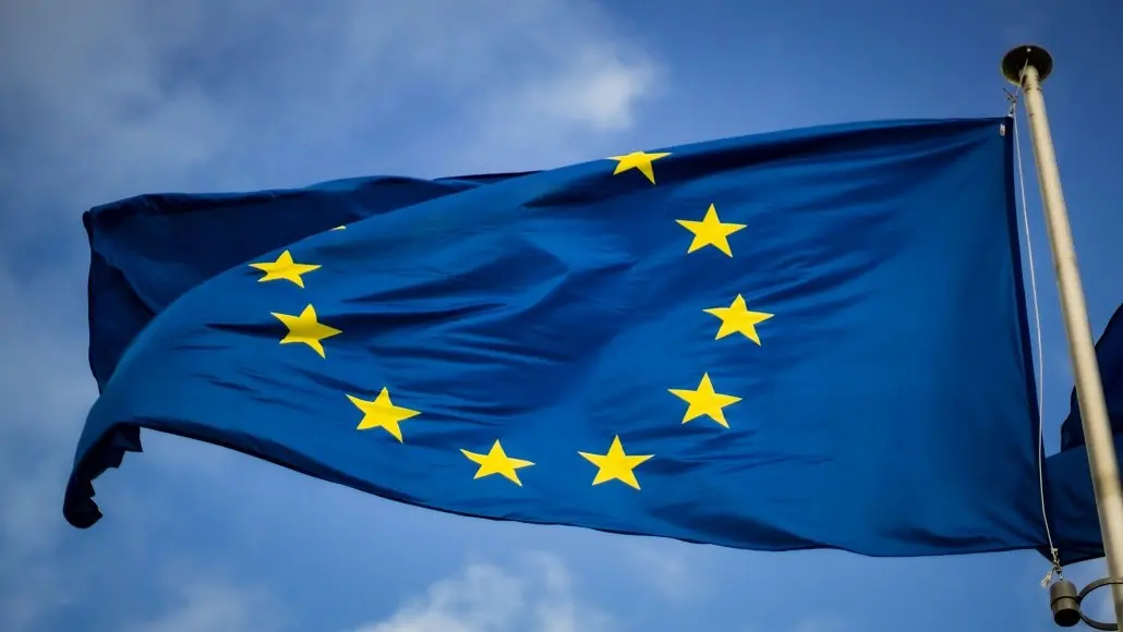 European Union flag waving on a bright blue sky with a circle of twelve yellow stars