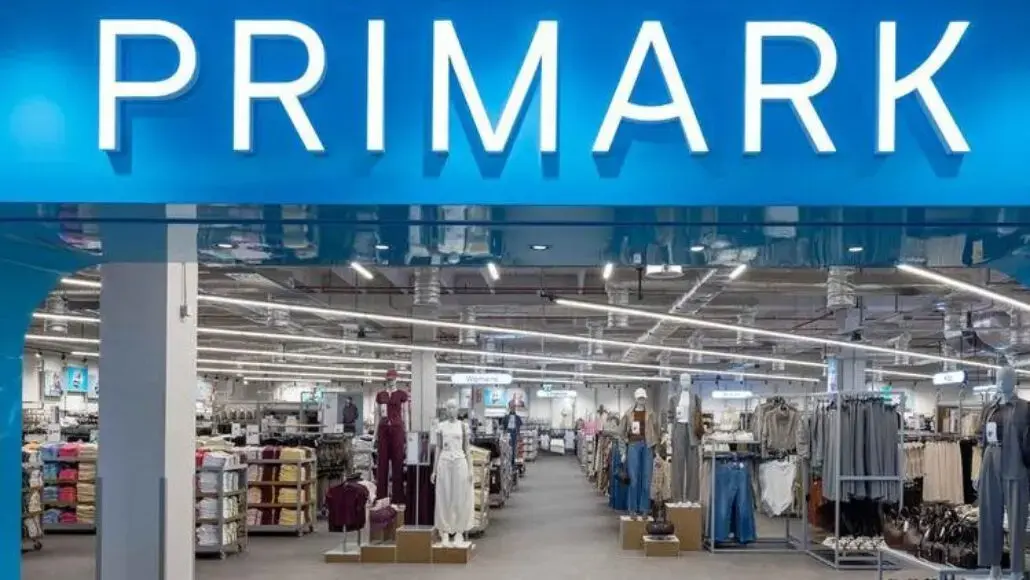 Primark store entrance with bright blue sign and well-lit clothing aisles inside.