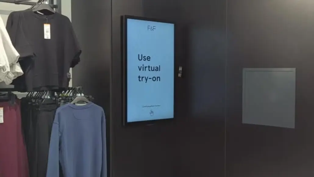 Digital sign in a clothing store reads 'Use virtual try-on' beside clothing racks.