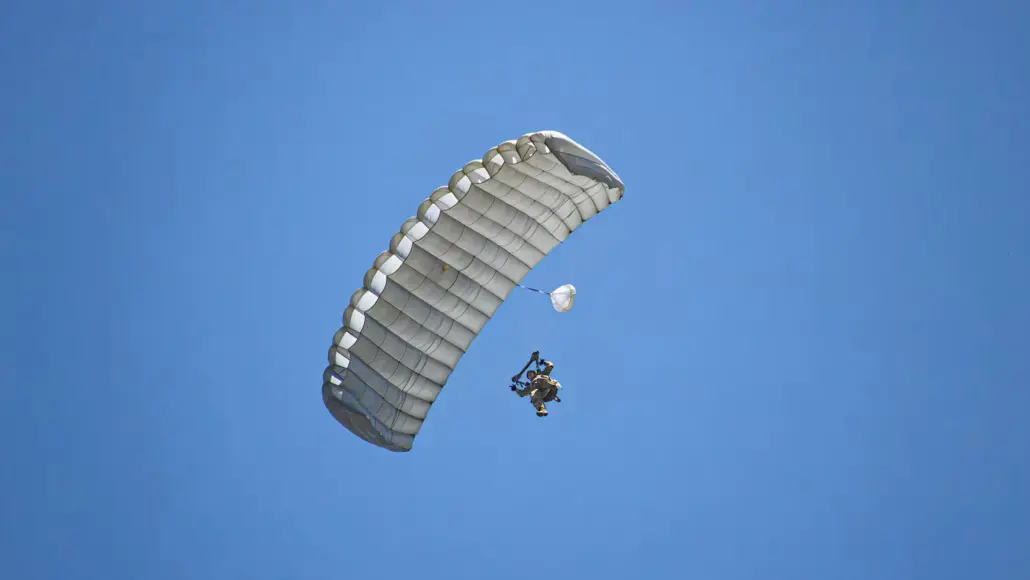 Tandem skydivers under a large white parachute against a bright blue sky.