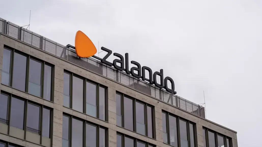 Zalando logo on the top of a modern glass-front office building against a gray sky.