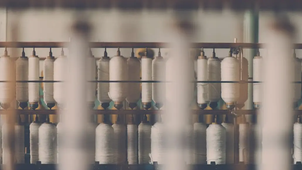 Rows of white yarn spools on a weaving loom in a textile factory setting.