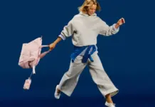 Old Navy Sport Launches as a Dedicated Activewear Destination Woman in a gray hoodie and wide-leg pants leaps mid-air, pink backpack swinging behind her against a blue background.