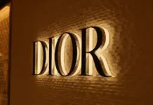 Christian Dior Plans Restructuring of LVMH Holding Structure Dior logo illuminated on a textured wall inside a warm-lit storefront.