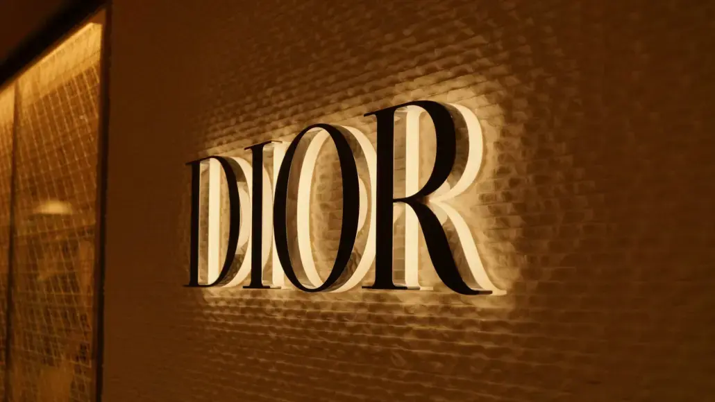 Dior logo illuminated on a textured wall inside a warm-lit storefront.