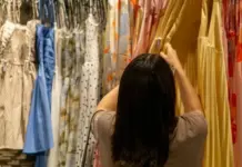 Global Apparel Resale Market Set to Hit $338.4 Billion in 2026 Back view of a person with dark hair in a beige top choosing a yellow dress from a rack of colorful dresses in a clothing store.