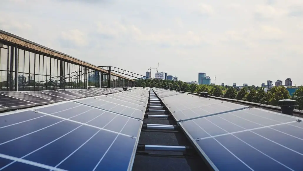 Row of solar panels on a rooftop with a city skyline in the distance.