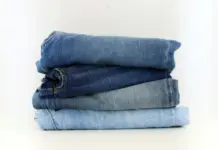 Denim Deal Partners with United Repair Centre to Advance Circular Denim at Scale Stack of folded blue jeans in varying washes on a white surface.