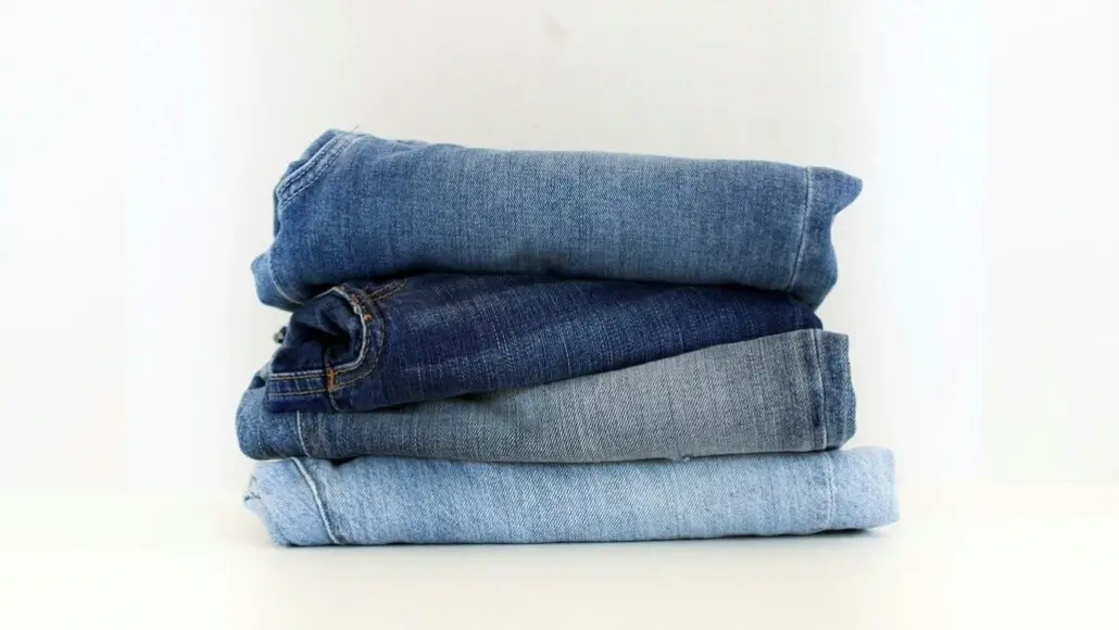 Stack of folded blue jeans in varying washes on a white surface.