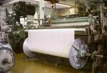 China Industrial Profits Rise 11.2% YoY in July, Textile Industry Up 7.9% Industrial textile loom feeding a wide white fabric roll through machines in a factory setting.