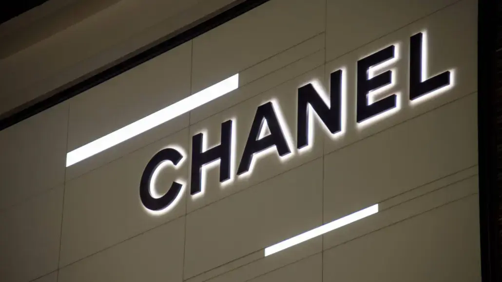 CHANEL logo on a light tiled wall with bold black letters and subtle backlighting.