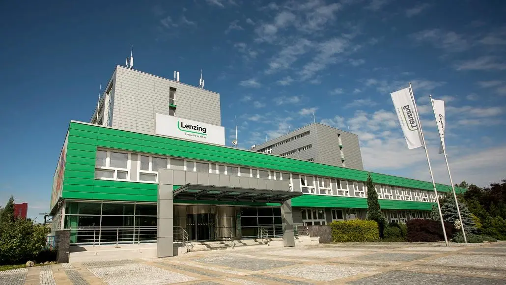 Modern corporate building with green siding, glass entrance, and a Lenzing sign on the facade under a blue sky.