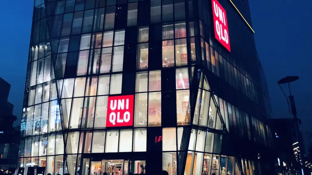 Nighttime view of a glass-front UNIQLO store with illuminated red UNIQLO logos on the facade.