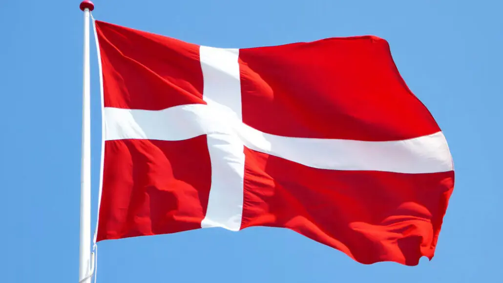 Danish flag waving on a white flagpole against a clear blue sky