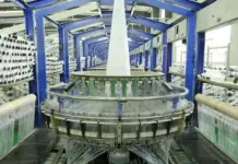 Spinnova Signs €1.5M Loan Deal With Yarn Spinner Tearfil Circular knitting loom in a textile factory, blue steel frame with yarns feeding from spools on both sides.