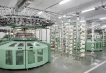 Argentina’s Textile Industry Faces Deep Structural Stagnation as Output Falls Over 22% Green circular knitting machine in a modern textile factory, with multiple yarn spools and overhead threading infrastructure.